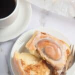 Gluten Free Glazed Cinnamon Roll on a plate next to a cup of coffee