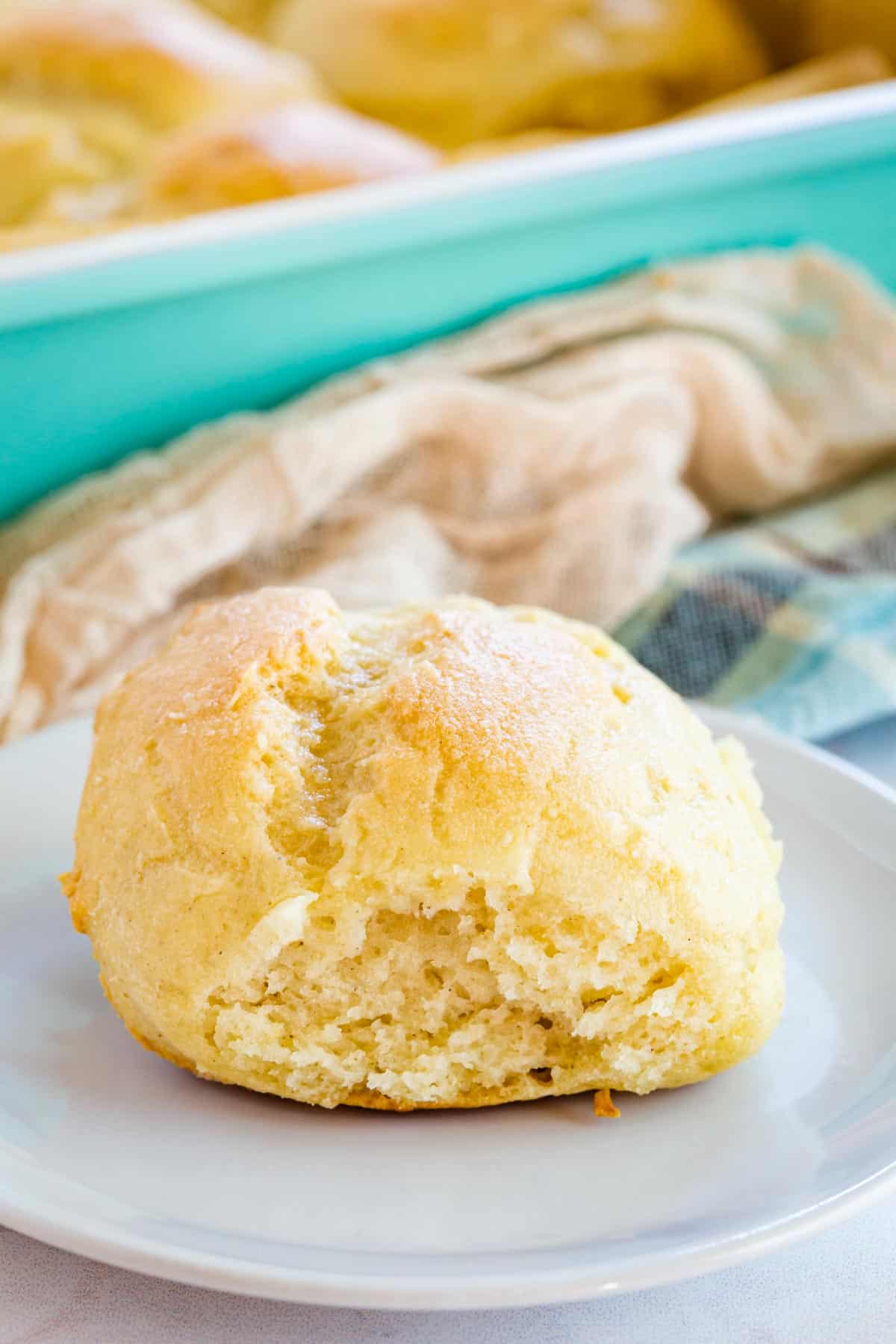 one dinner roll on a white plate with the baking pan behind it