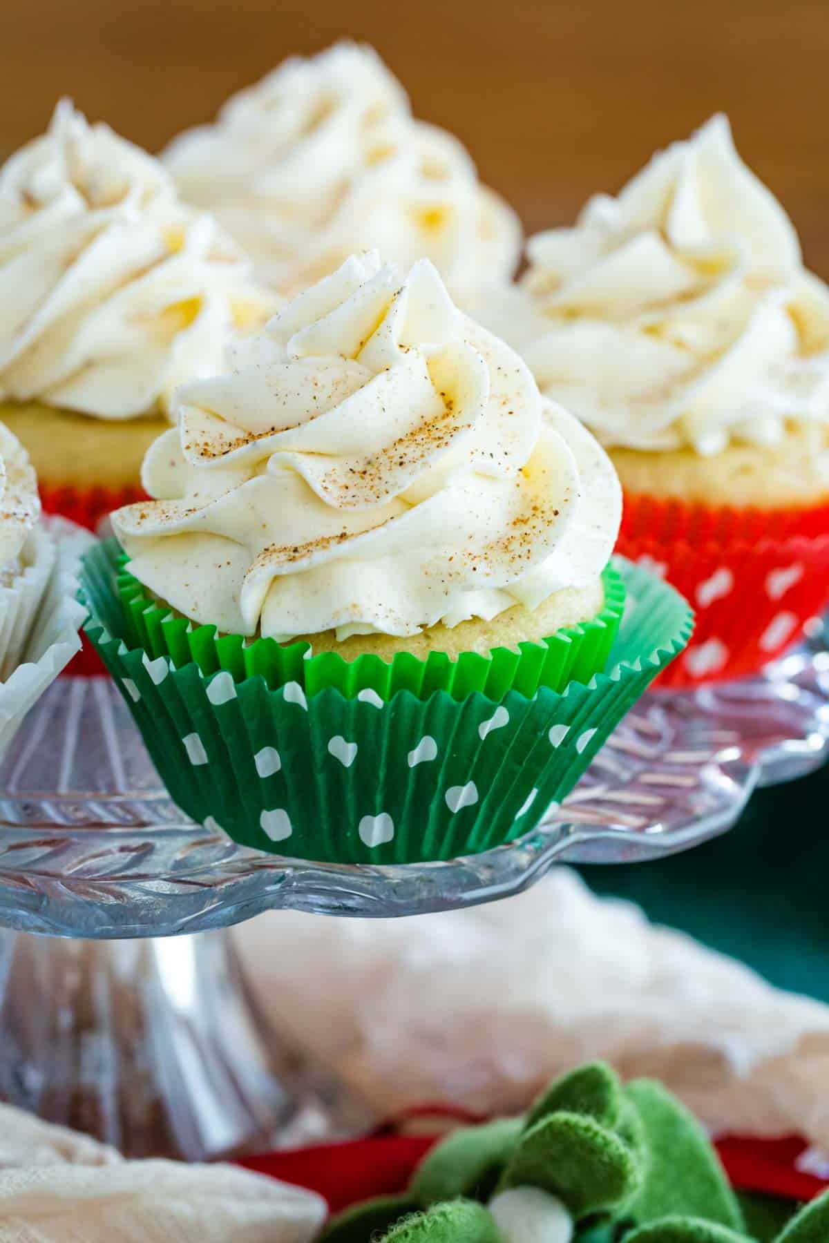 eggnog cupcakes in colorful wrappers on a glass cake stand