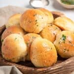 a wooden bowl of gluten free rolls topped with garlic herb butter