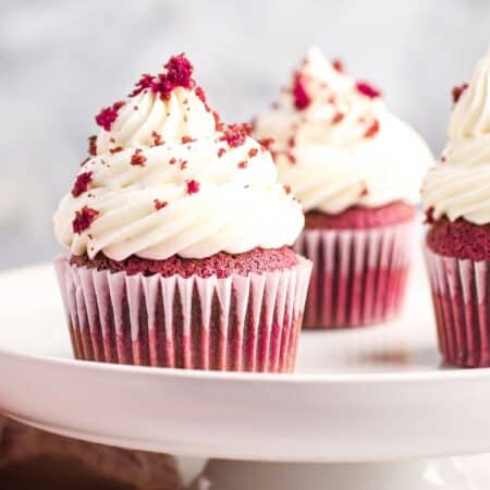 three red velvet cupcakes with cream cheese frosting on a small cake stand