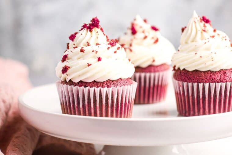 three red velvet cupcakes with cream cheese frosting on a small cake stand