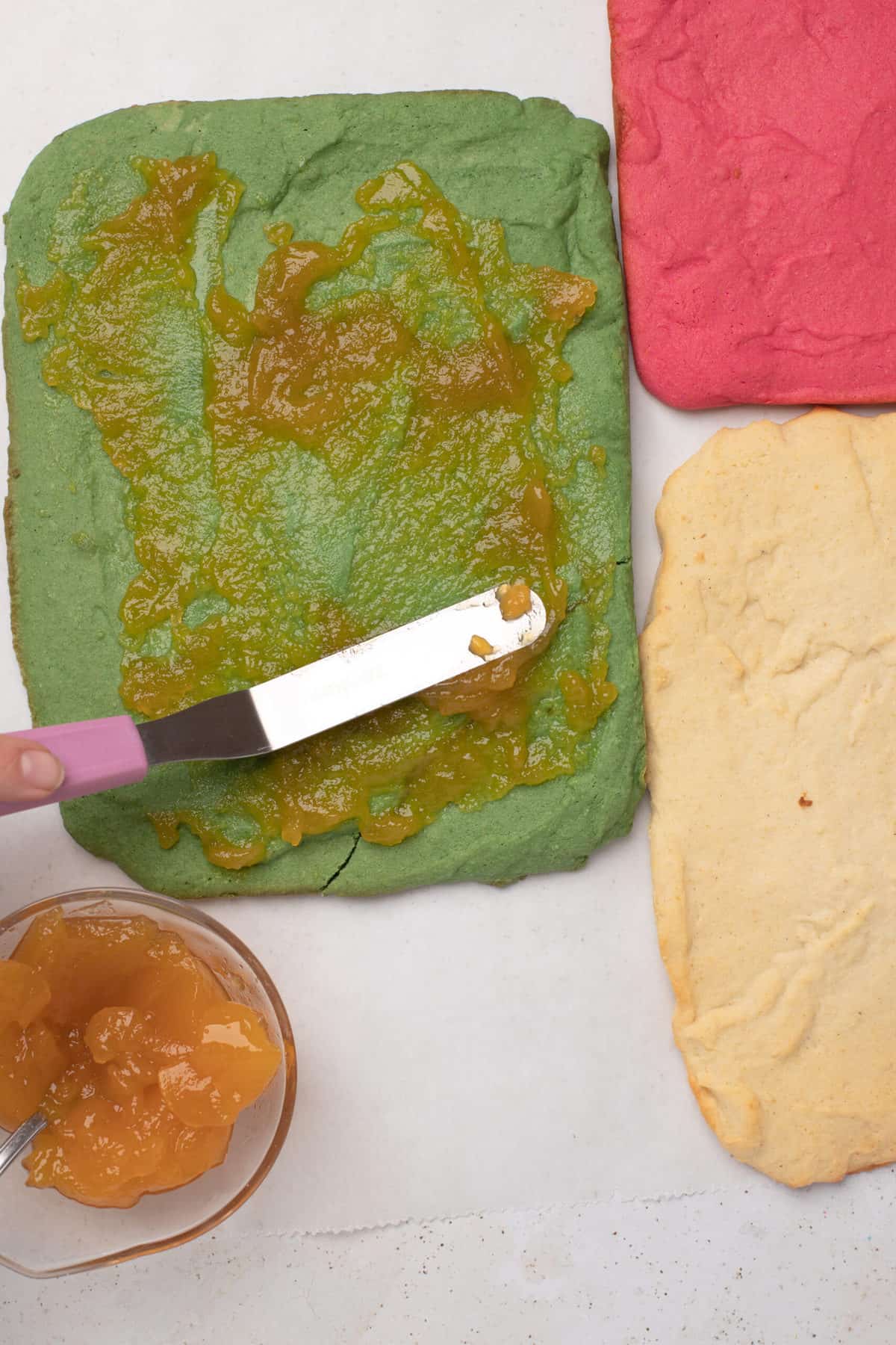 brushing jam on a green sponge cake