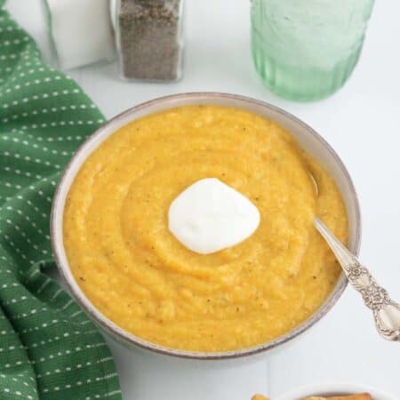 a bowl of creamy vegetable soup on a table with a green napkin and a bowl of crackers