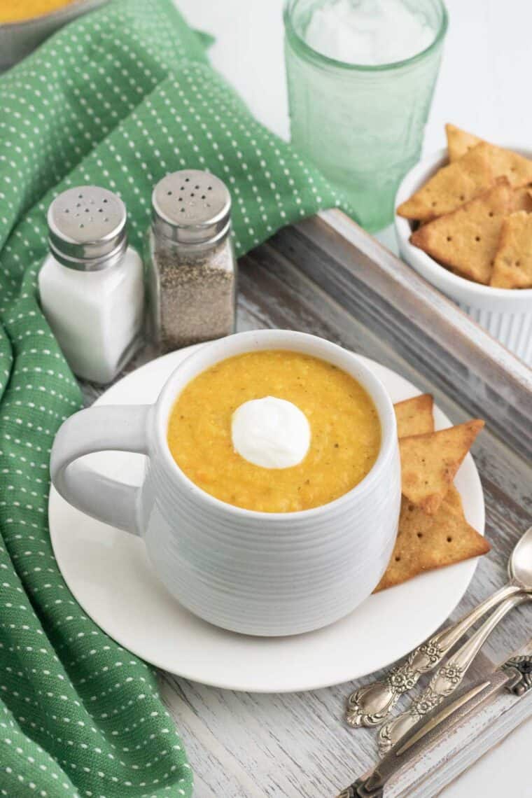 a mug of creamy soup on a saucer with crackers