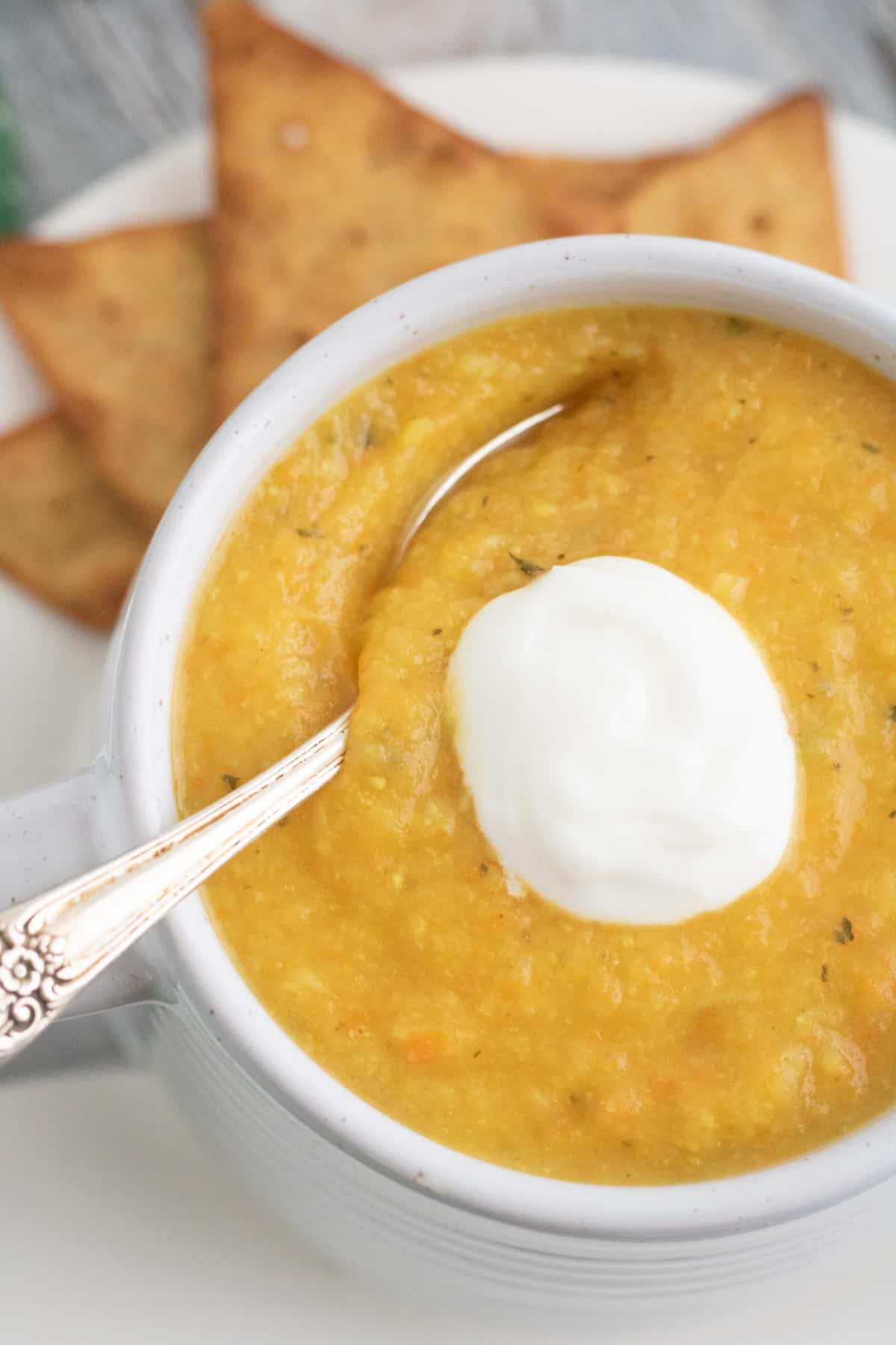 spoon resting in a mug of creamy vegetable soup with greek yogurt on top