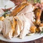 carved roast turkey on a serving platter with sprigs of fresh herbs