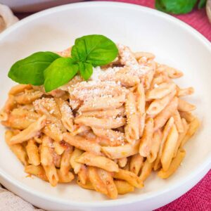 A bowl of penne covered with vodka sauce and parmesan cheese, garnished with a sprig of basil.