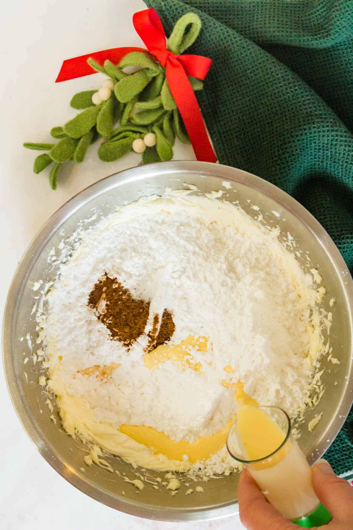 adding powdered sugar to a mixing bowl with eggnog frosting