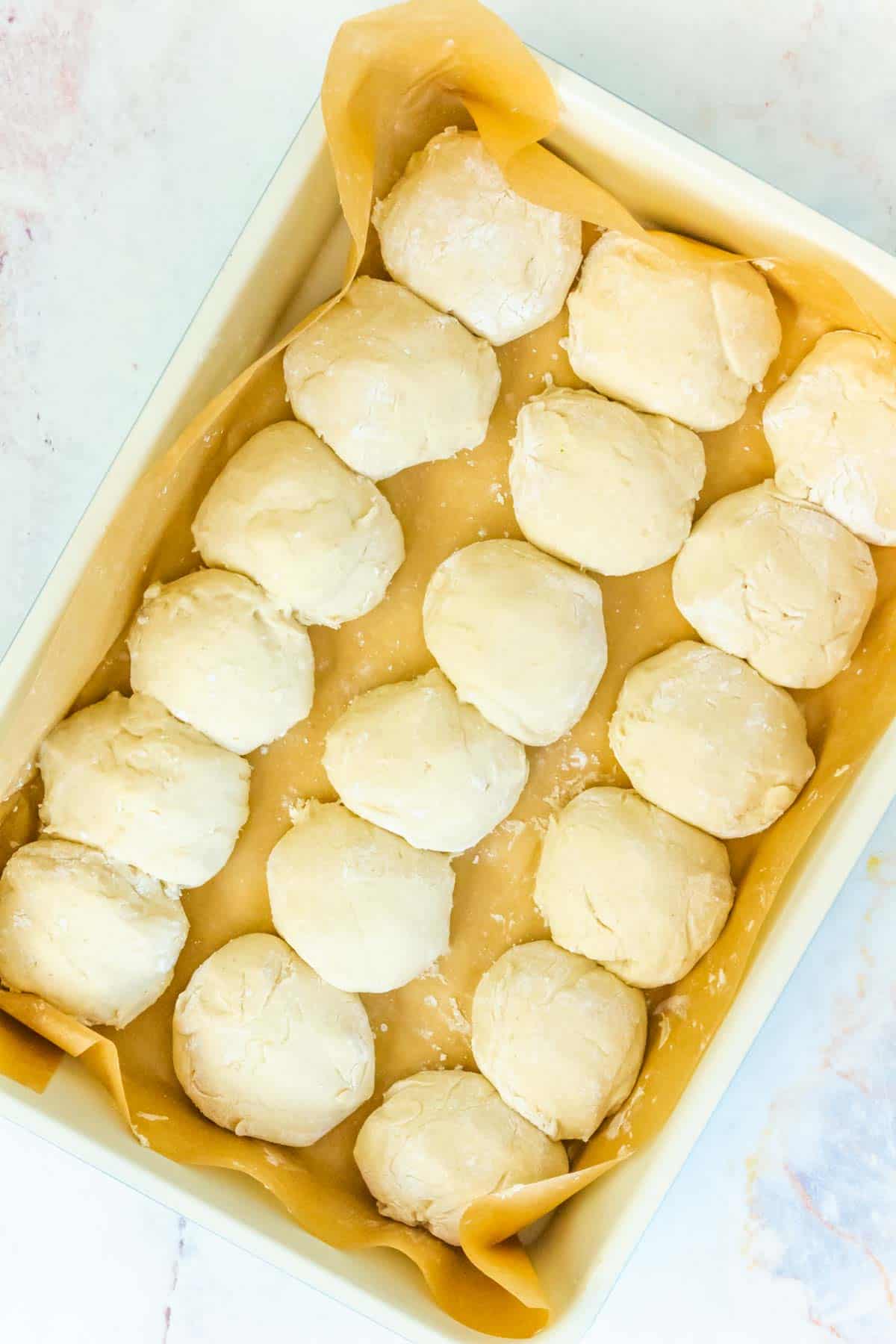 unbaked balls of dinner roll rough in a parchment-lined baking pan