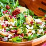 tossed salad with orange slices, pomegranate seeds, nuts, and feta in a wooden bowl