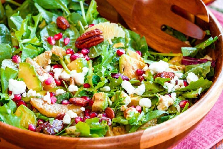 tossed salad with orange slices, pomegranate seeds, nuts, and feta in a wooden bowl