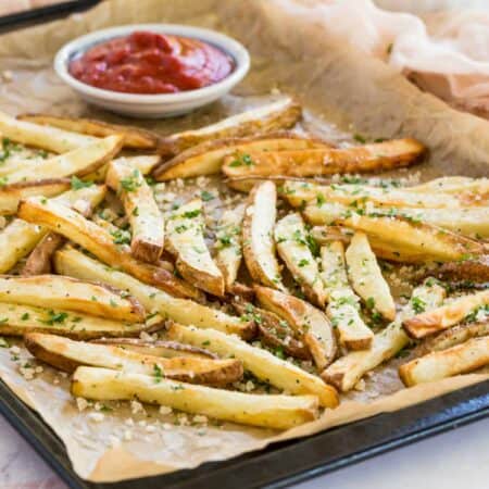 french fries on a parchment lined baking sheet sprinkled with parmesan cheese and parsley
