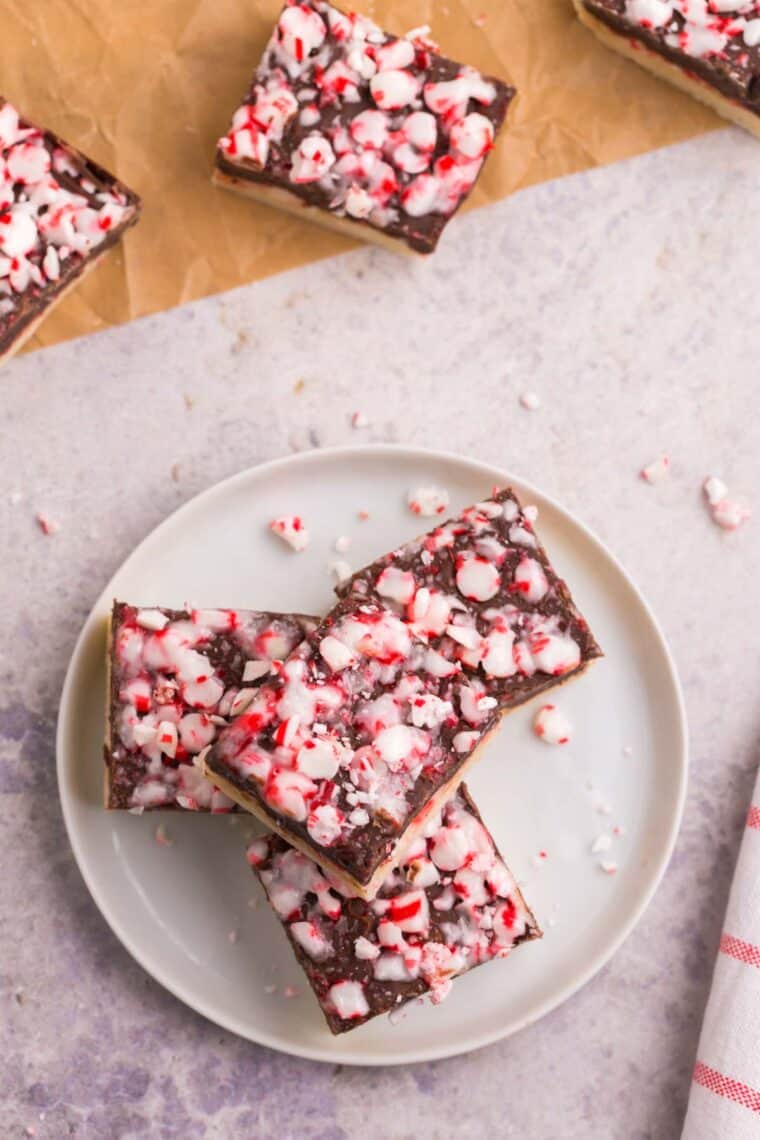 four squares of peppermint fudge topped with candy cane pieces on a white plate
