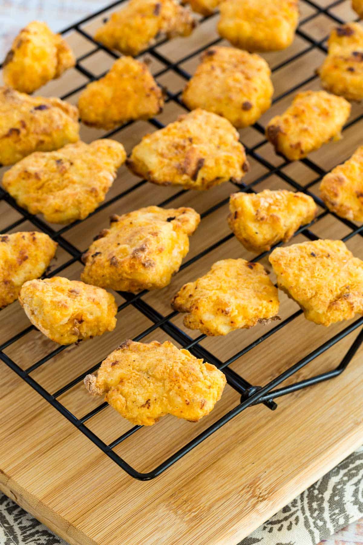 Finished air fryer chicken nuggets are laid out on a wire rack to cool.