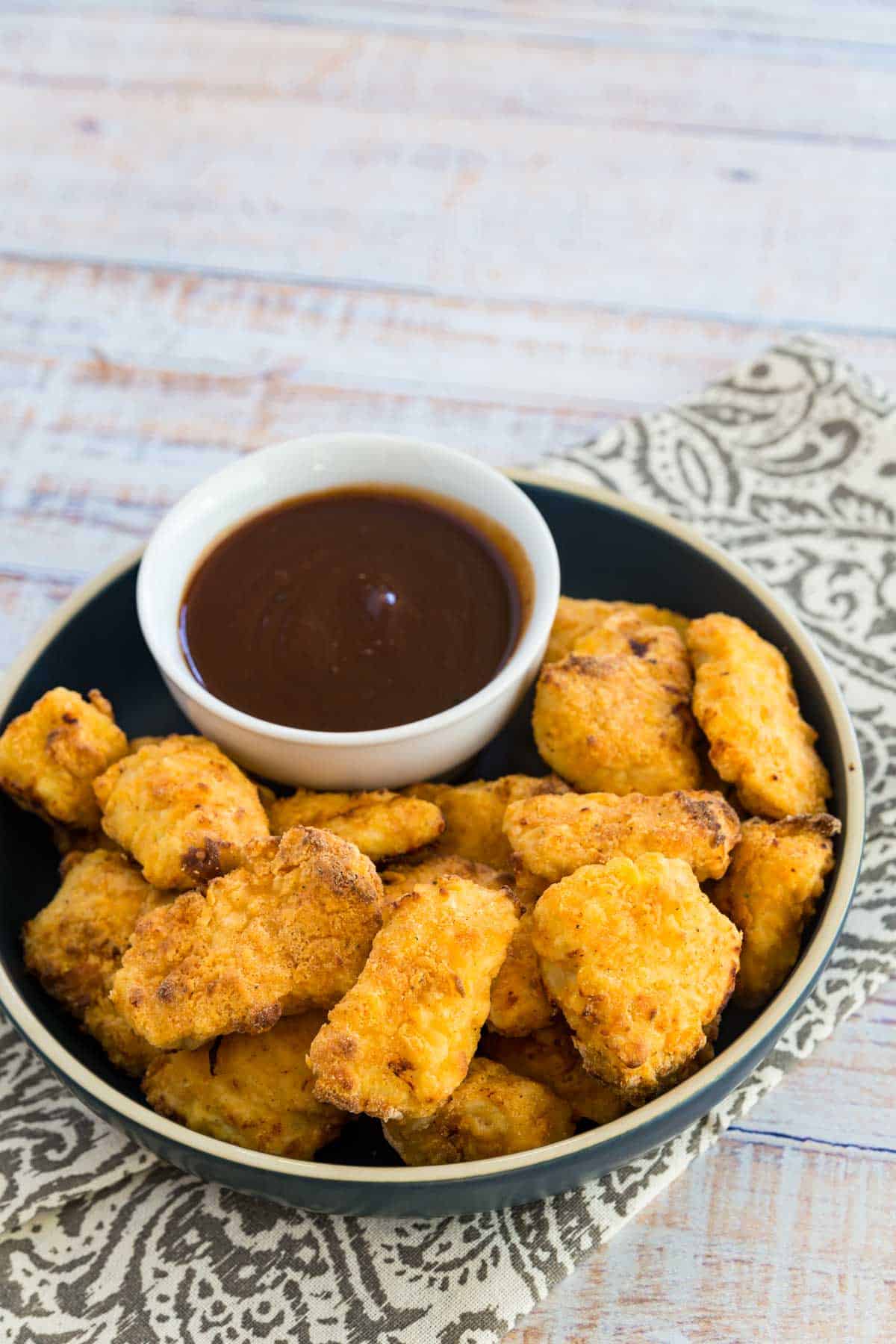 Crispy air fryer chicken nuggets on a plate next to BBQ dipping sauce.
