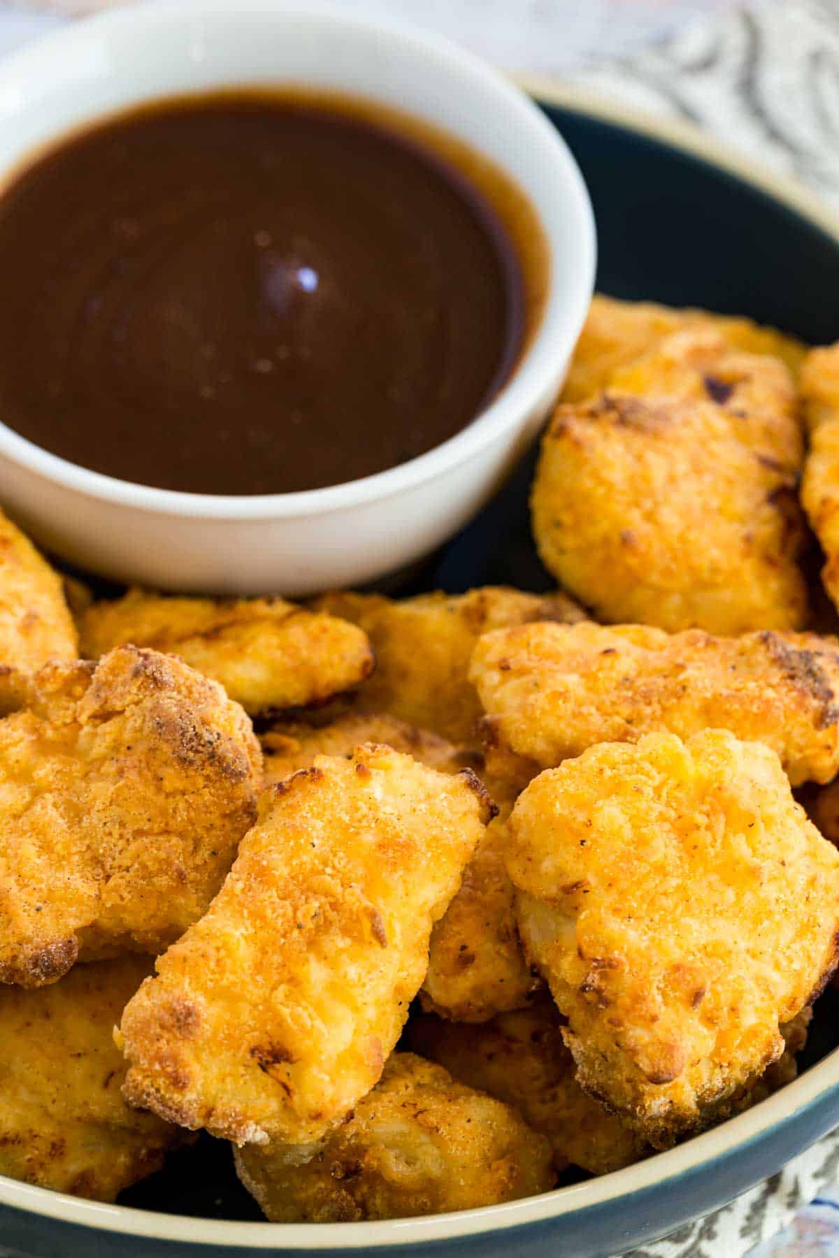 Crispy air fryer chicken nuggets on a plate next to BBQ dipping sauce.