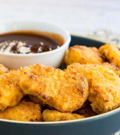 Crispy air fryer chicken nuggets on a plate next to BBQ dipping sauce.