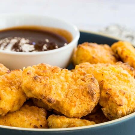 Crispy air fryer chicken nuggets on a plate next to BBQ dipping sauce.