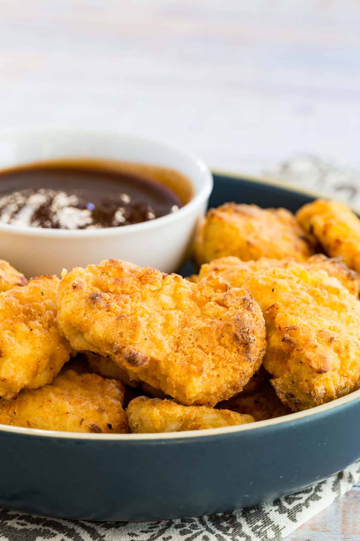 Crispy air fryer chicken nuggets on a plate next to BBQ dipping sauce.