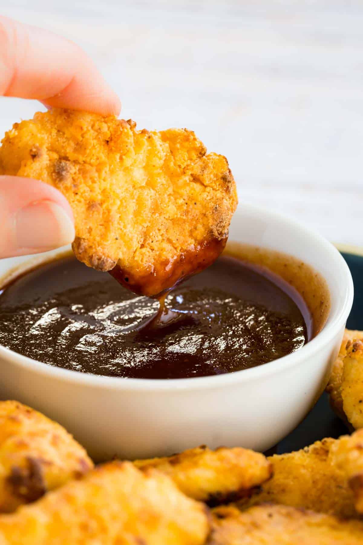 An air fried chicken nugget is dipped into BBQ sauce.