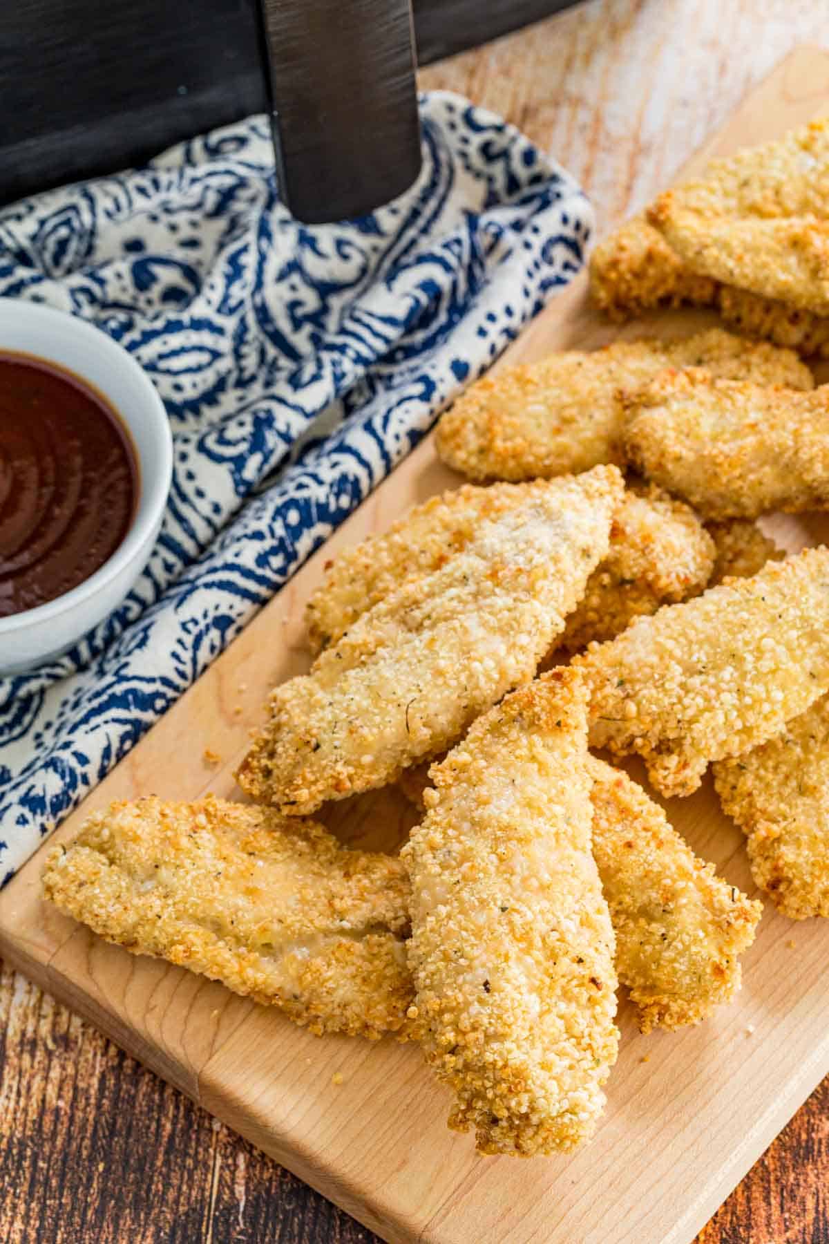 Air fryer chicken tenders served next to a bowl of BBQ sauce for dipping.