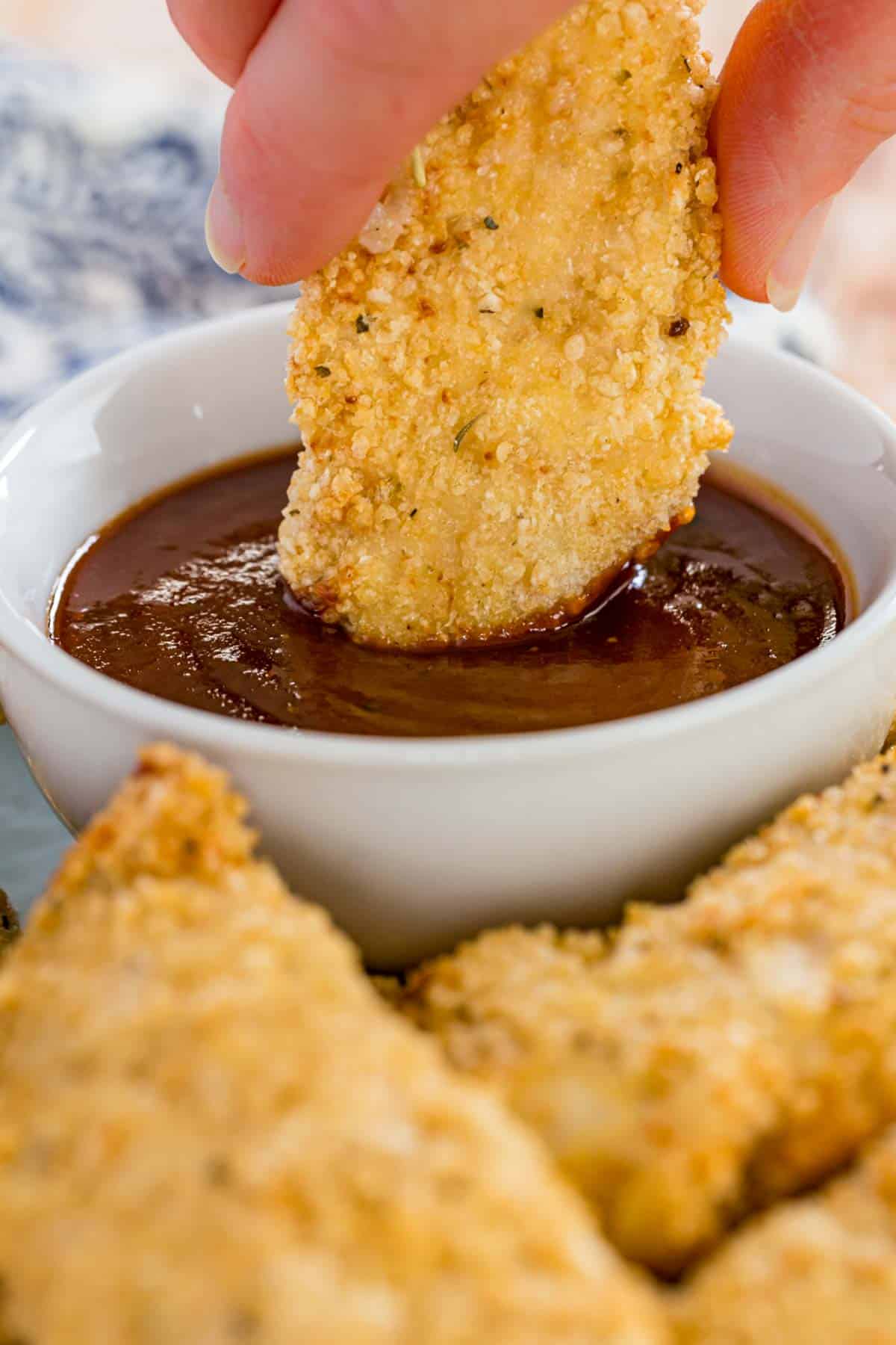 An air fryer chicken tender is dipped into BBQ sauce.