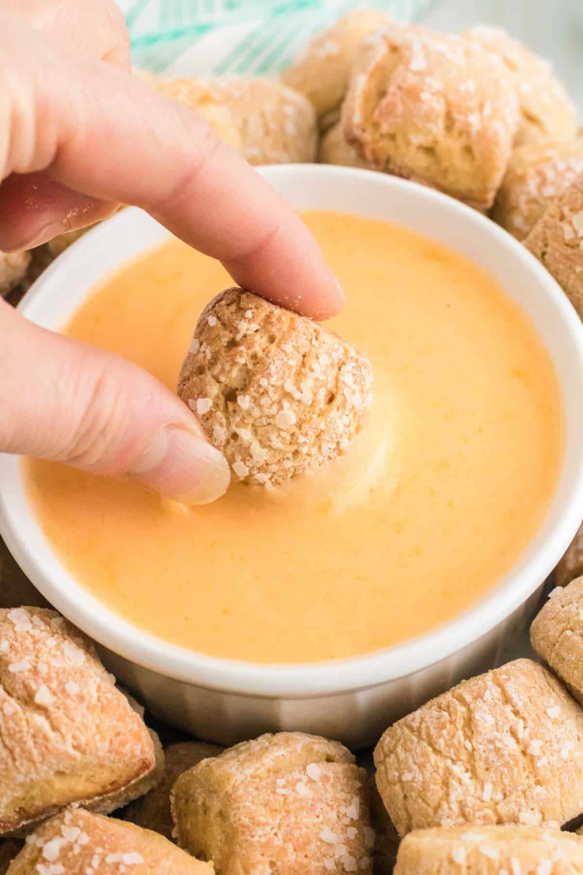 A pretzel nugget is dipped into a bowl of cheese sauce.