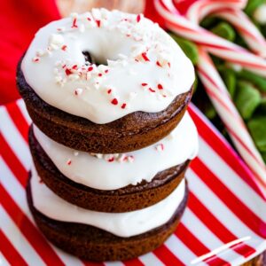 three chocolate donuts with white icing on a red and white striped plate