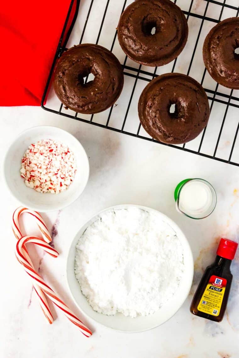 chocolate donuts on a cooling rack next to the ingredients to make peppermint icing