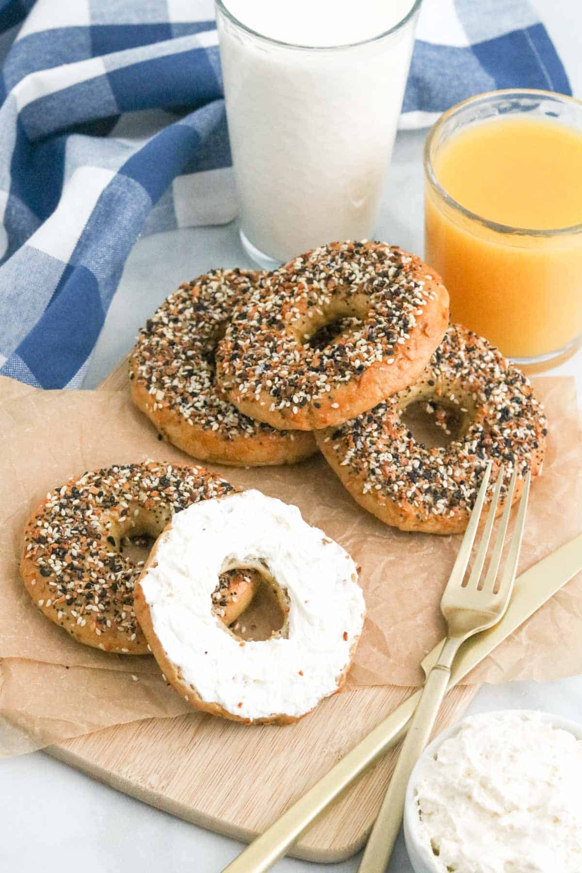 Gluten free Everything bagels, with one sliced open and spread with cream cheese.