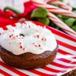 baked chocolate donut with peppermint icing and candy cane pieces on top on a red and white striped plate
