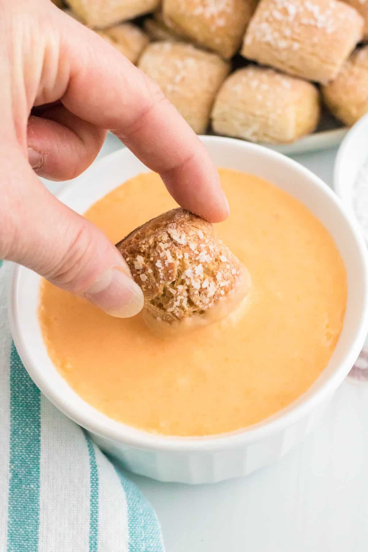 A pretzel nugget is dipped into cheese sauce.