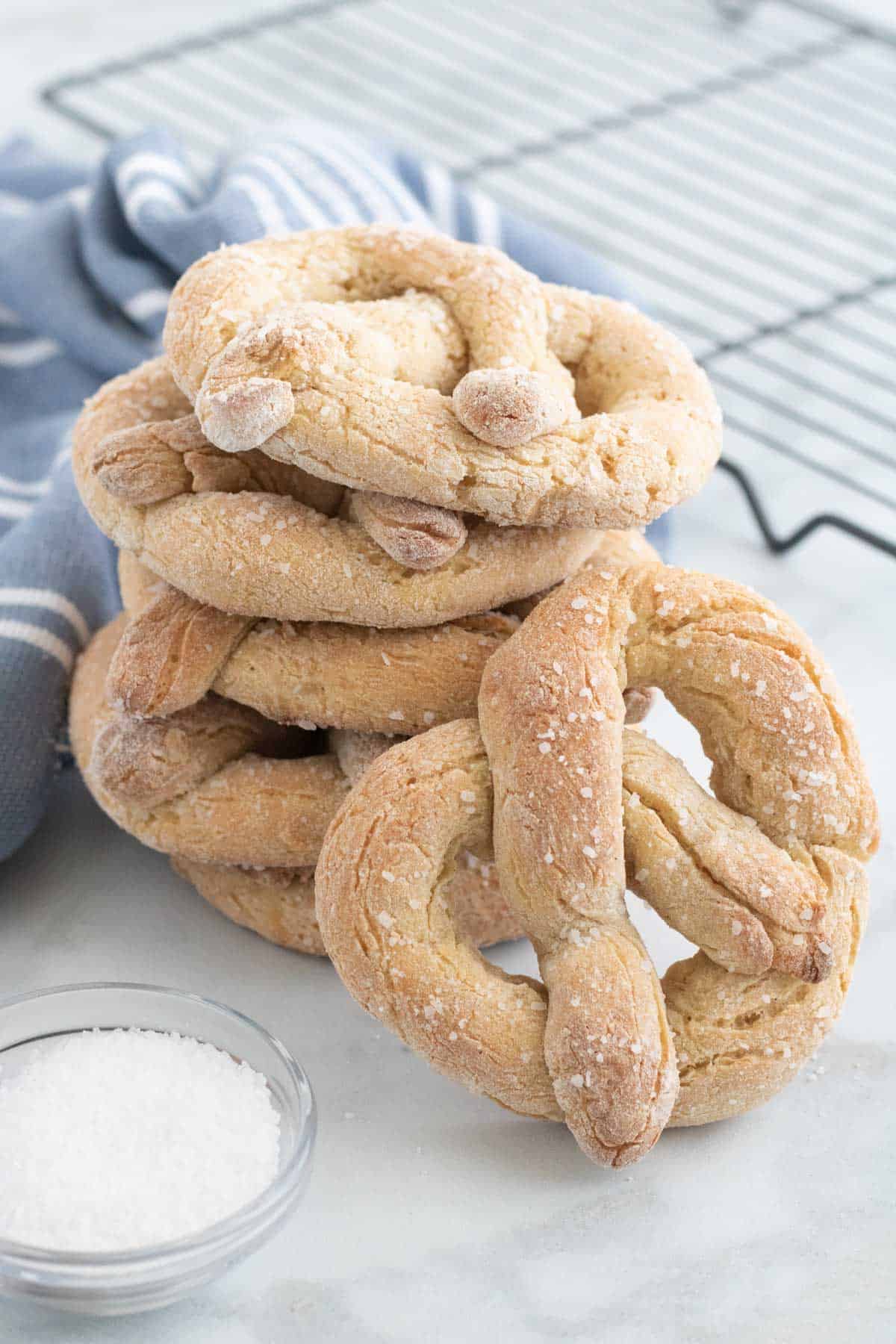 A stack of gluten free soft pretzels next to a bowl of coarse salt.