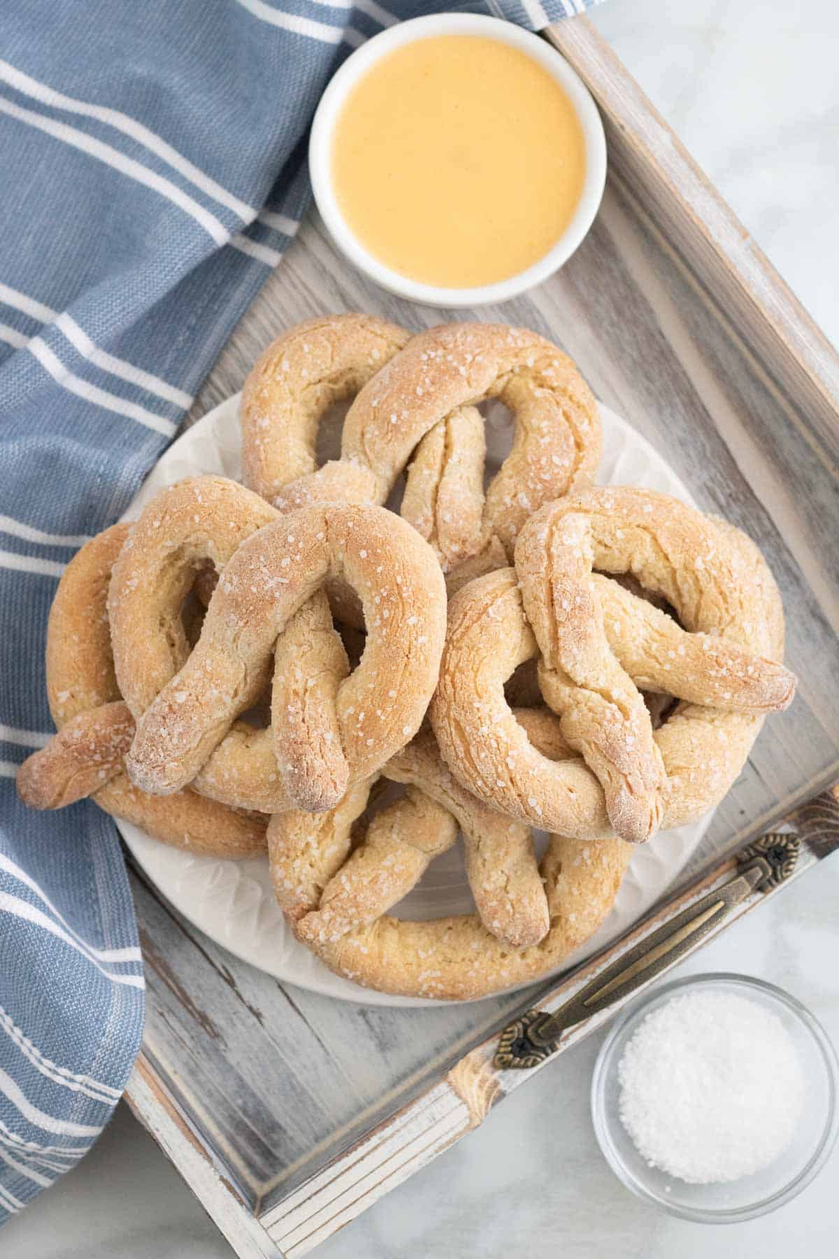 Soft pretzels on a plate, next to a bowl of coarse salt and another bowl of melted butter.