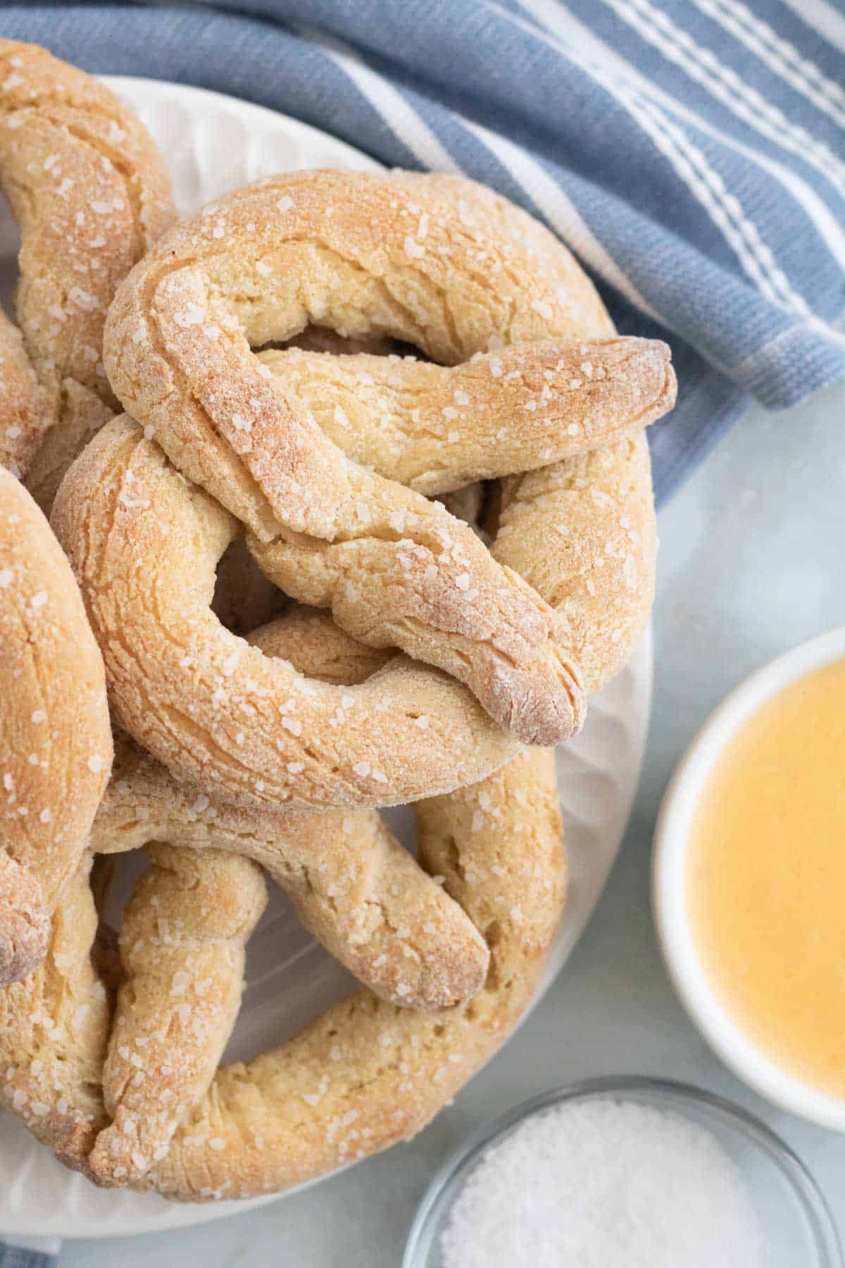 Gluten free soft pretzels stacked on a plate, next to butter and salt.