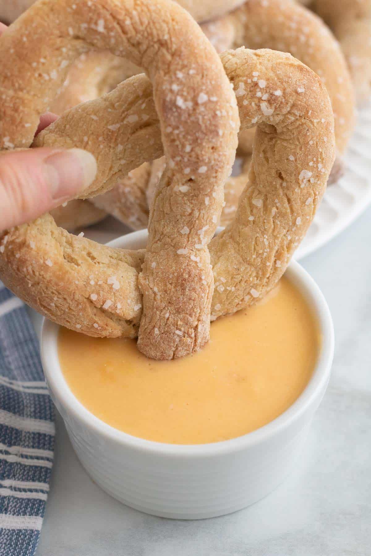 A homemade gluten free pretzel is dipped into cheese sauce.