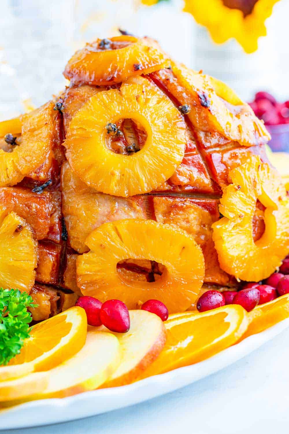 glazed ham covered with pineapple rings on a serving platter surrounded by fruit garnishes
