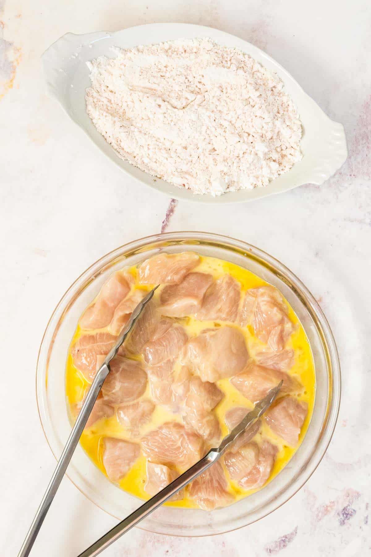 Marinated chicken pieces are placed in an egg wash for coating.