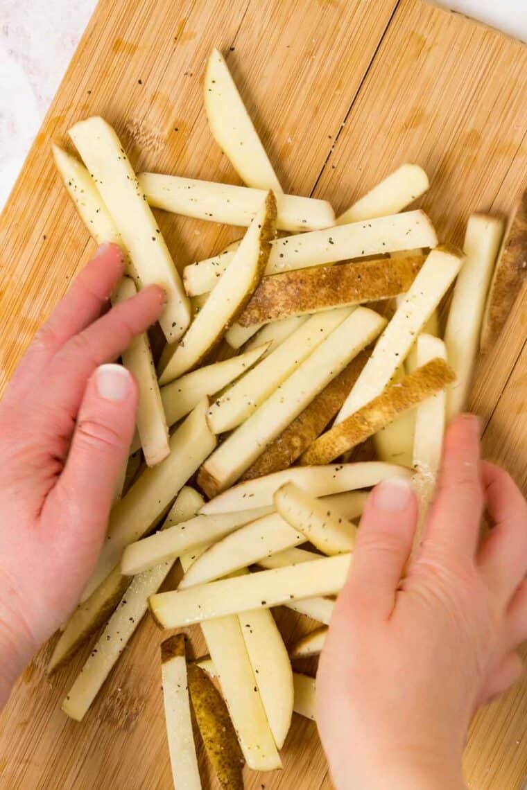 tossing raw potatoes cut into fries in oil, salt, and pepper