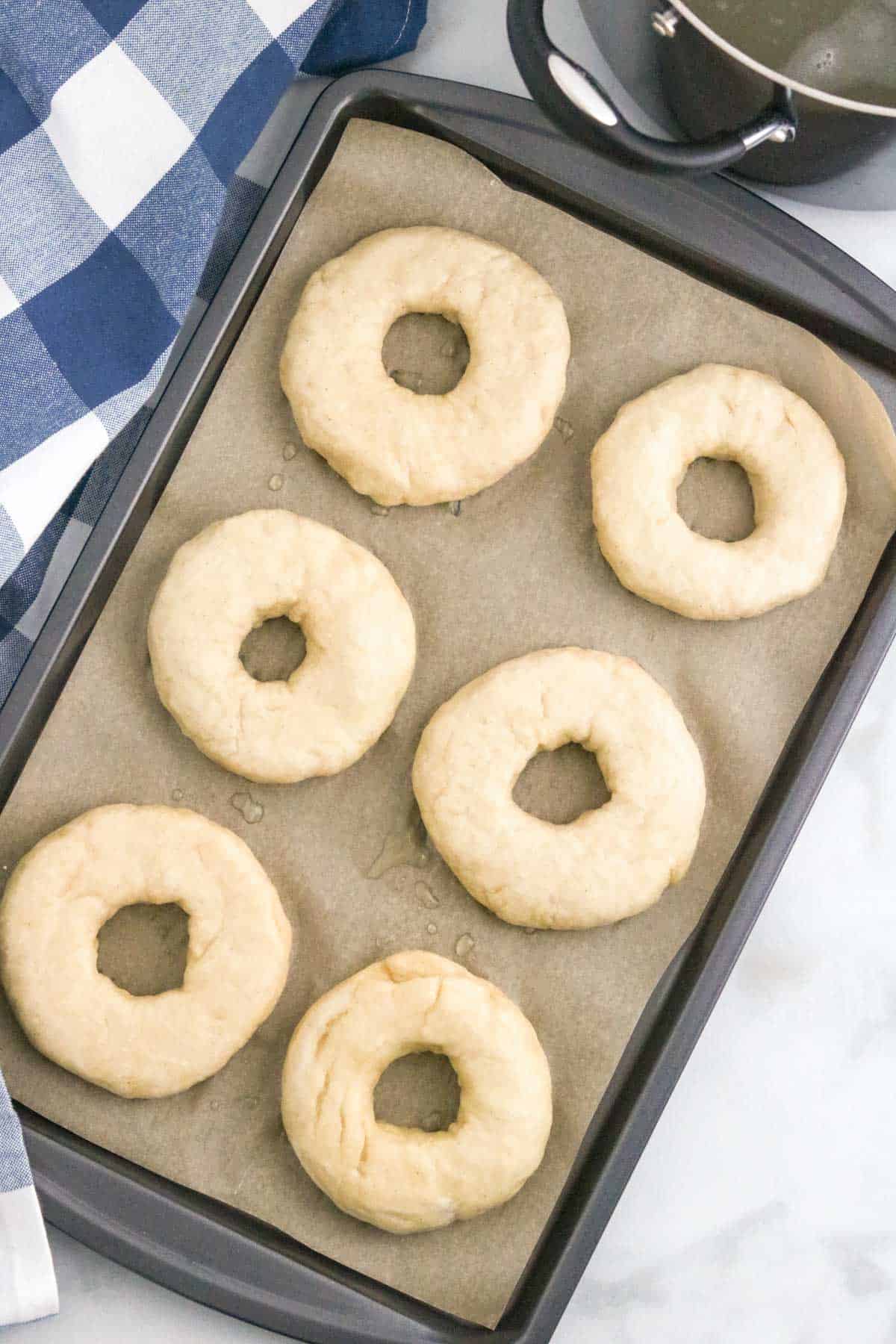 Boiled bagels on a lined baking sheet.