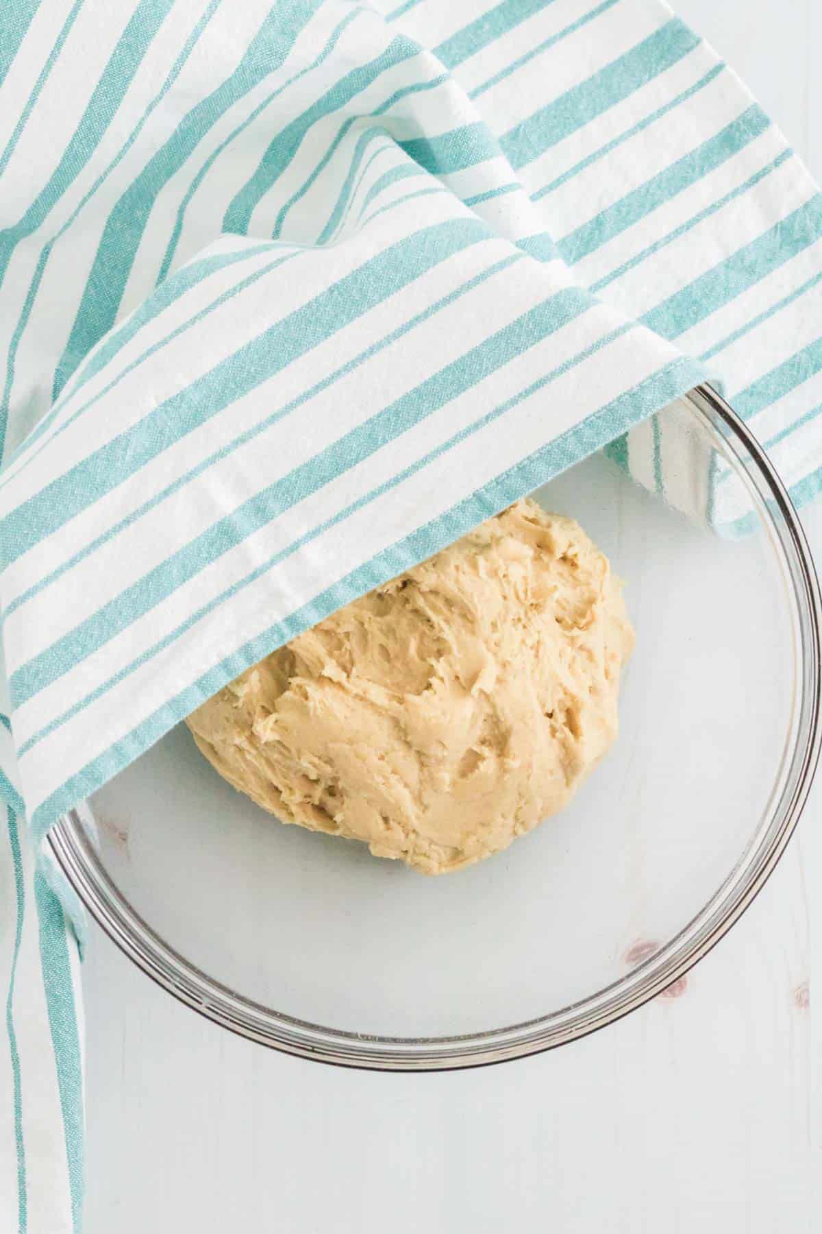 Pretzel dough is left to rise in a greased mixing bowl, covered with a cloth.