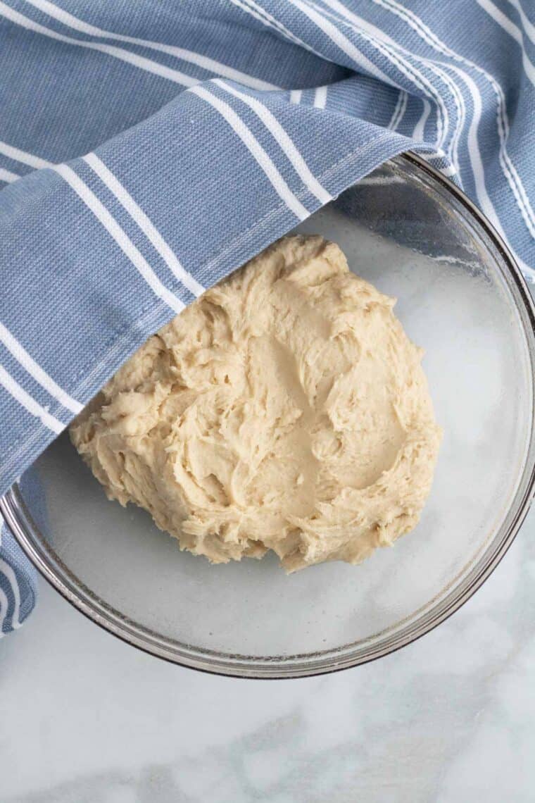 Gluten free pretzel dough is left in a bowl to rise, covered with a cloth.