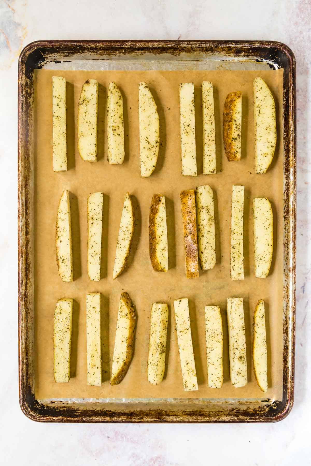 Three rows of seasoned french fries on a piece of parchment paper over a metal baking sheet