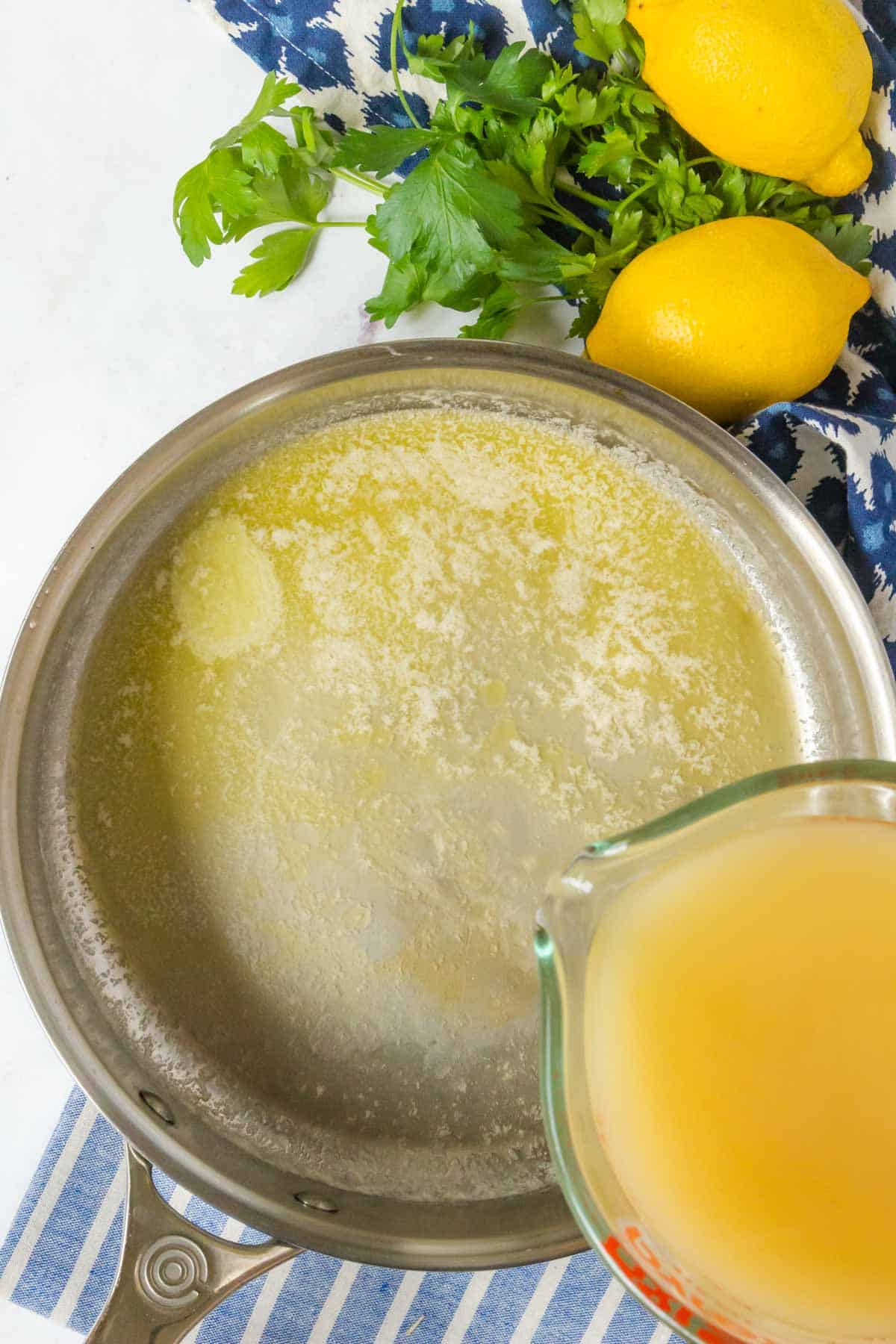 A cornstarch and chicken broth slurry being poured into a skillet full of melted butter