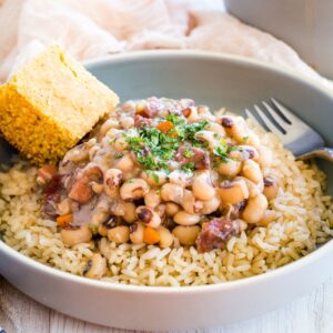 a bowl of black eye peas over rice with a hunk of cornbread