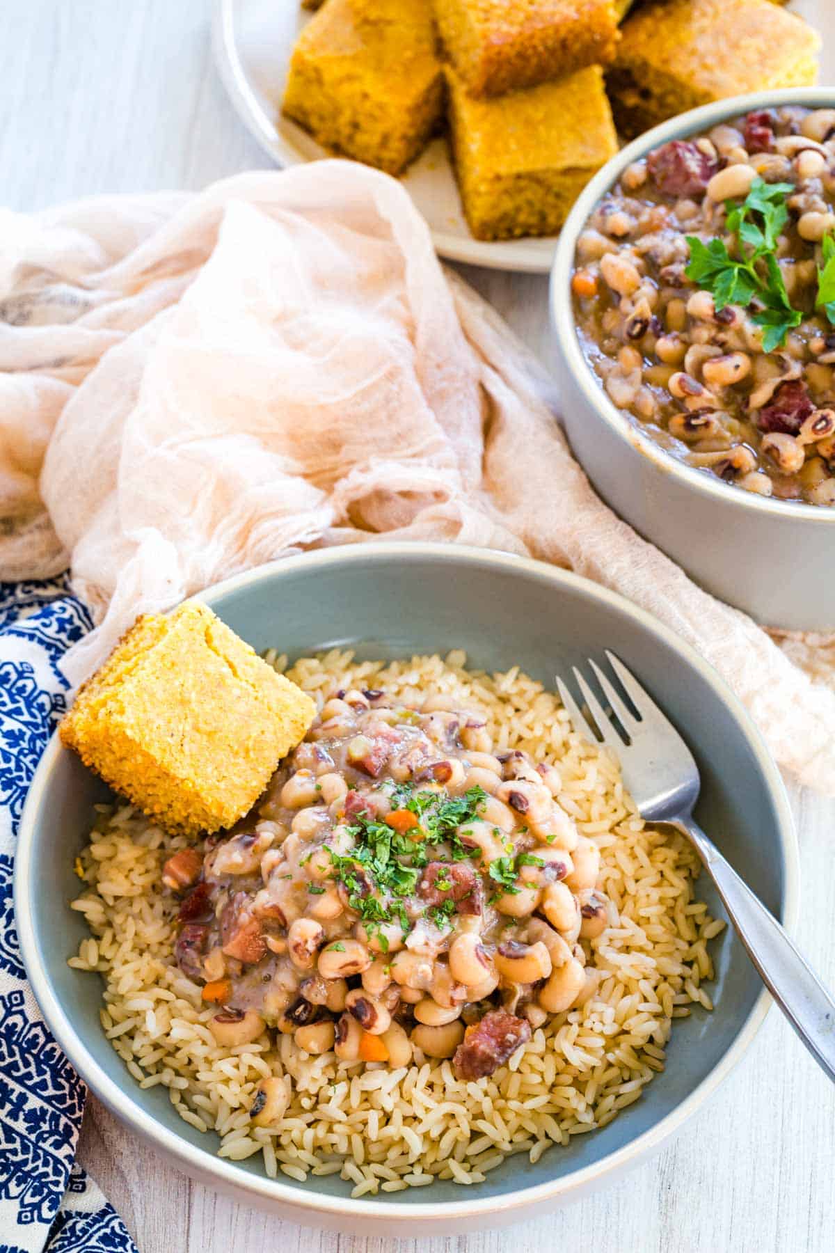 A bowl of black eyed peas next to serving dishes with corn bread.