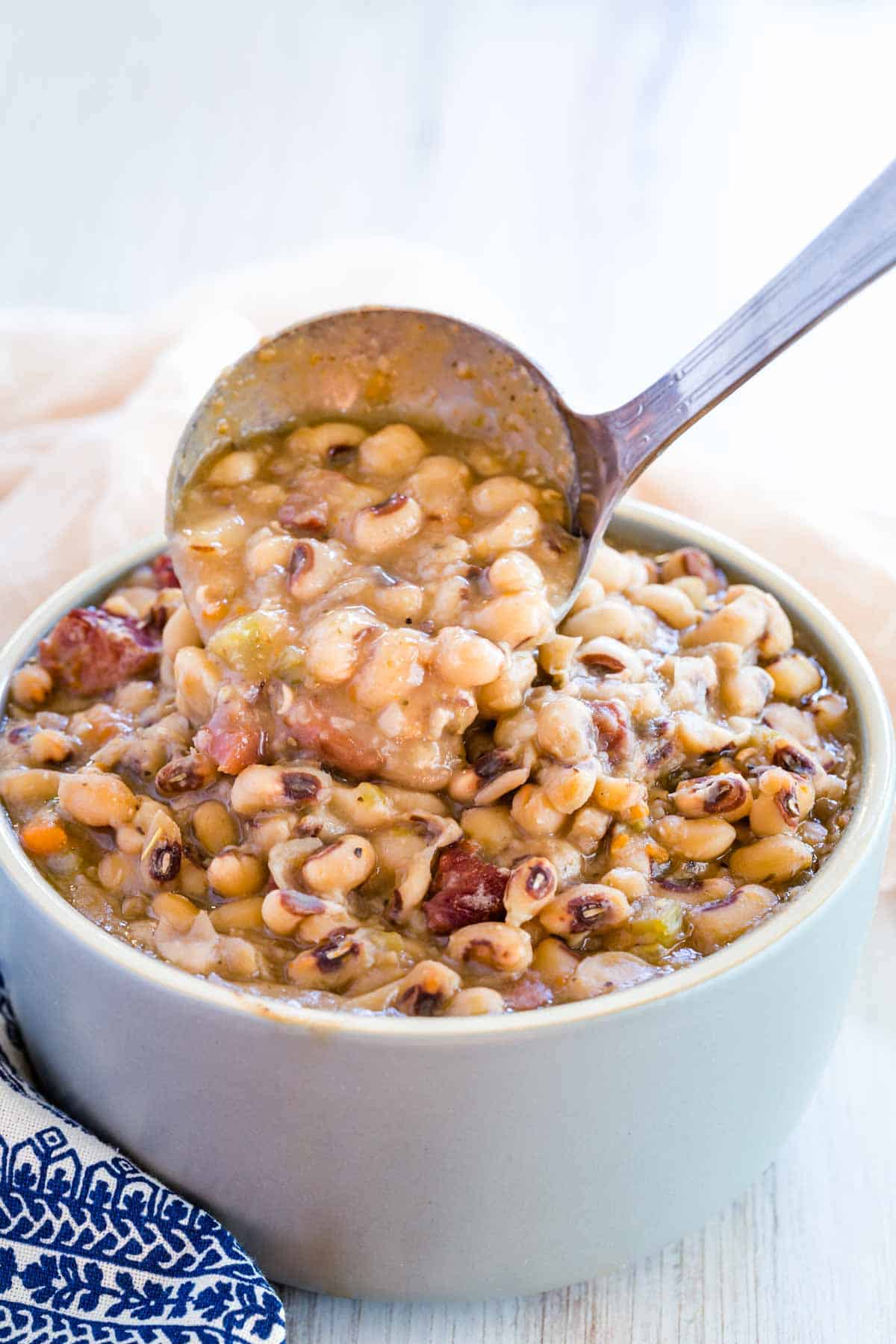 A ladle is used to serve up black eyed peas in a bowl.