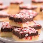 four squares of peppermint fudge topped with candy cane pieces on a white plate