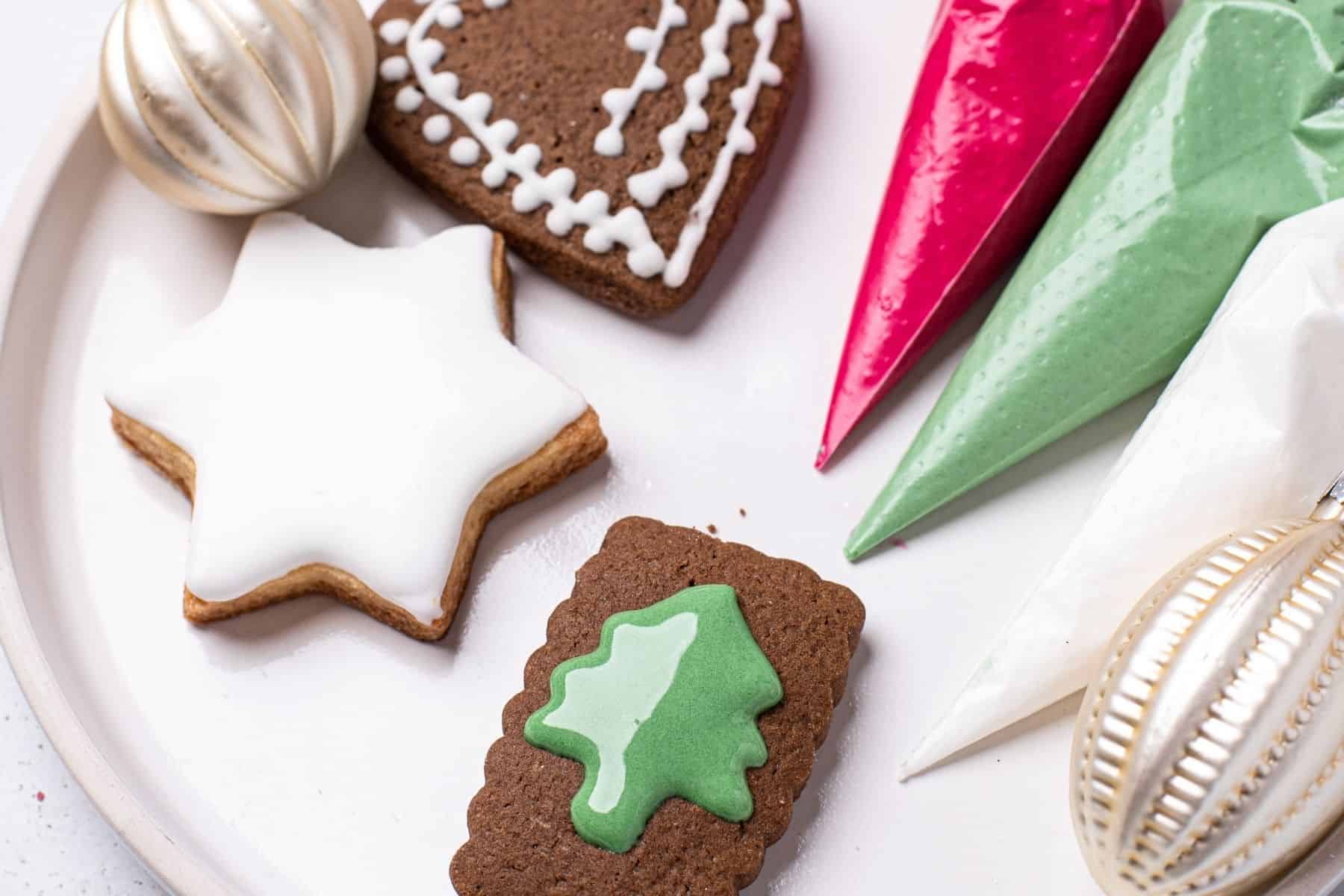 piping bags of colored royal icing and three decorated cookies on a plate